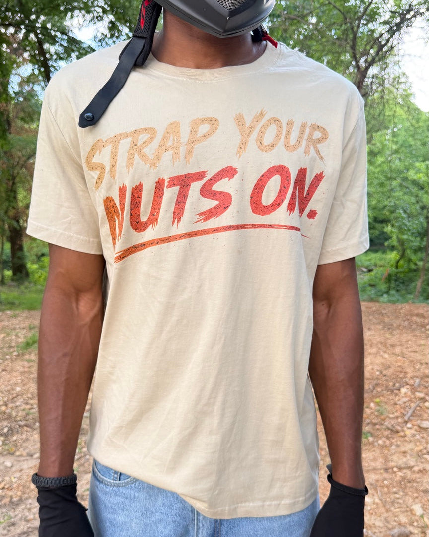 Person wearing a t-shirt with 'STRAP YOUR NUTS ON' text, standing outdoors.