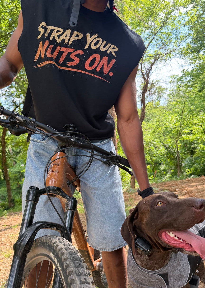 Person on a bike with a dog, wearing a black sleeveless shirt with text, in a forest setting.