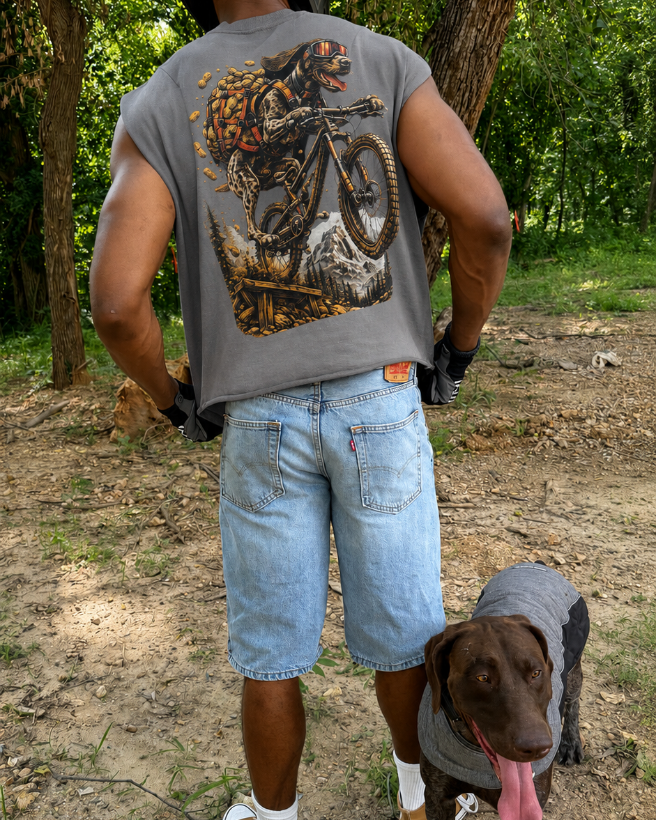 Person wearing a sleeveless shirt with a graphic design and a dog in a gray sweater standing on a dirt path.